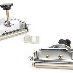 K&ouml;nnte beinhalten: Zwei Metallkantenschneider mit schwarzen Kn&ouml;pfen und silberner Hardware. Ein Trimmer hat eine Schraube zur Einstellung, der andere Fl&uuml;gelmuttern. Ein kleines silbernes Metallteil ist ebenfalls enthalten.