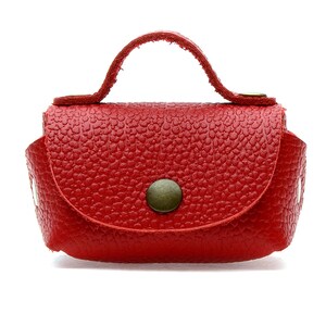 May include: A small, red leather handbag with a textured surface. The bag features a curved flap secured by a round, bronze-colored button. It has a small handle and is designed to be carried by hand.