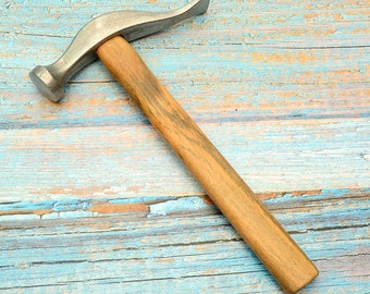 May include: A metal forming hammer with a curved head and a wooden handle. The hammer's head is silver, and the handle is a light brown colour. The tool is designed for shaping metal and other materials.