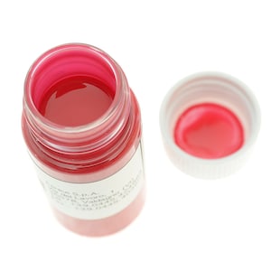May include: A clear glass bottle filled with bright red liquid, with a white cap next to it. The bottle's contents are visible, and the cap is off, revealing the same red color inside. The bottle has a label.