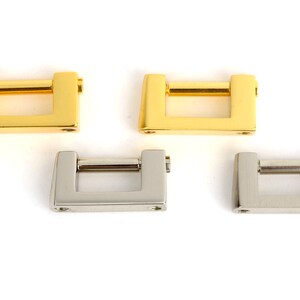 May include: Four metal rectangular clasps in gold and silver tones. Each clasp has a rectangular frame with a horizontal bar and two small holes. The clasps are displayed on a white background.
