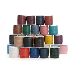 May include: A collection of colorful leather cord spools in various shades, including red, blue, green, and brown. The spools are stacked in a pyramid shape against a white background. Ideal for crafting and jewelry making.