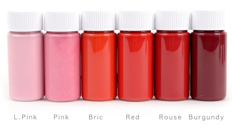 May include: Six small bottles filled with shades of red and pink liquid, labeled L. Pink, Pink, Bric, Red, Rouse, and Burgundy. Each bottle has a white cap. The bottles are arranged in a row against a white background.