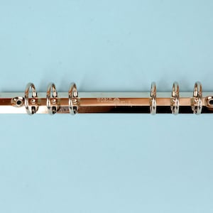 May include: Close-up of a silver metal binder mechanism with six rings. The binder is set against a light blue background. The text "WORLD STAR" is visible on the metal strip.