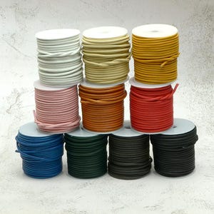 May include: A collection of spools of colorful cord in various shades, including white, yellow, pink, orange, red, blue, green, and black. The cords are neatly wound on white spools, offering a range of options for crafting and jewelry making.