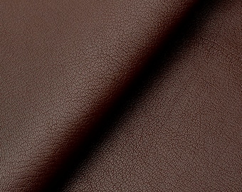 May include: Close-up of a sheet of dark brown leather. The leather has a textured surface with a subtle grain pattern. The material is folded, creating shadows and highlighting the depth of the color.
