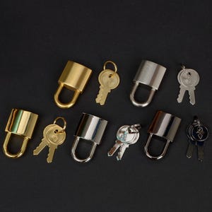 Peut inclure: Plusieurs cadenas et clés de différentes couleurs métalliques, dont l'or et l'argent. Les clés sont conçues pour correspondre aux serrures. L'image est posée sur un fond sombre, mettant en valeur les détails de la quincaillerie de sécurité.