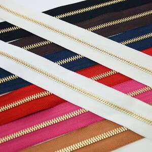Puede incluir: Surtido de cremalleras de colores con dientes dorados. Las cremalleras son de varios colores, incluyendo blanco, negro, marr&oacute;n, azul marino, rojo, rosa y beige. Las cremalleras est&aacute;n dispuestas en diagonal.