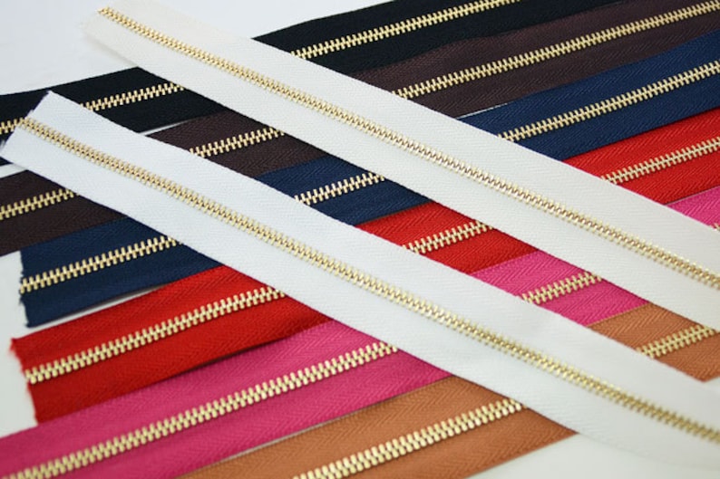 Puede incluir: Surtido de cremalleras de colores con dientes dorados. Las cremalleras son de varios colores, incluyendo blanco, negro, marr&oacute;n, azul marino, rojo, rosa y beige. Las cremalleras est&aacute;n dispuestas en diagonal.