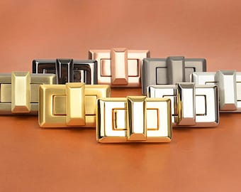 May include: A collection of rectangular metal clasps in various finishes, including gold, silver, and bronze. Each clasp features a central bar and a rectangular frame, suitable for bags or other accessories.