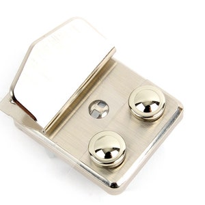 May include: A close-up of a silver-colored metal hinge with a rectangular base. The hinge has two round, shiny silver rivets and a rectangular top piece. The metal has a brushed finish.