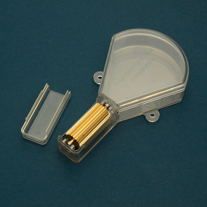 Puede incluir: Un recipiente de pl&aacute;stico transparente con tapa abatible, que contiene varias varillas met&aacute;licas de color dorado. La tapa est&aacute; parcialmente abierta y hay una peque&ntilde;a pieza de pl&aacute;stico transparente separada al lado. El fondo es de color verde azulado.