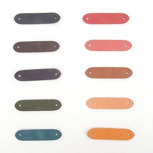 May include: A collection of ten leather tags in various colors, each with two pre-punched holes for attaching to items. Colors include black, brown, purple, green, and blue, paired with red, pink, tan, and orange.