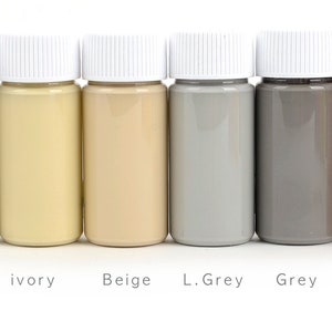 May include: Six small bottles of paint in a row, each with a white cap. The colors are white, ivory, beige, light grey, grey, and tan. The names of the colors are printed below each bottle.