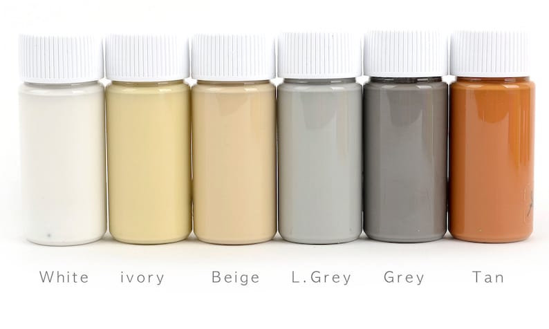 May include: Six small bottles of paint in a row, each with a white cap. The colors are white, ivory, beige, light grey, grey, and tan. The names of the colors are printed below each bottle.