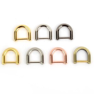 May include: Seven metal D-rings in various finishes: gold, silver, gunmetal, and rose gold. The D-rings are arranged in two rows, showcasing their different colors and metallic textures. These rings are used for bag making and other craft projects.