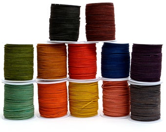 May include: A collection of spools of colorful suede cord in various shades, including black, brown, red, orange, yellow, green, and blue. The cords are neatly wound on white spools, creating a visually appealing display. Ideal for crafting and jewelry making.