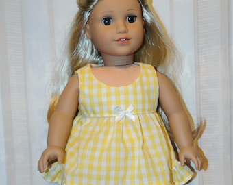 May include: A blonde doll wearing a yellow and white gingham dress with a white bow at the waist. The dress has a ruffled hem.