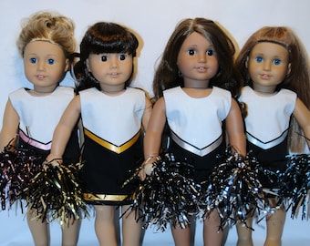 May include: Four dolls wearing black and white cheerleading outfits with gold and silver details. Each doll is holding a black and silver pom-pom.
