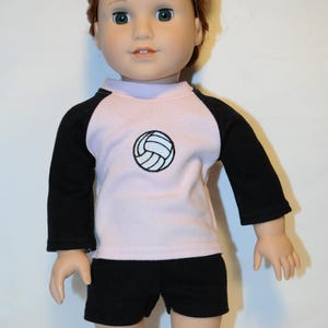 Puede incluir: Una mu&ntilde;eca con cabello casta&ntilde;o rojizo recogido en un mo&ntilde;o, que viste una camiseta de manga larga rosa claro con mangas ragl&aacute;n negras y un gr&aacute;fico de voleibol negro en el pecho, junto con pantalones cortos negros lisos. Tiene ojos verdes.