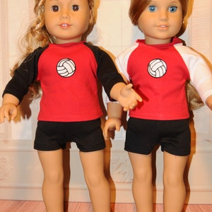Puede incluir: Dos mu&ntilde;ecas de piel clara, una con cabello rubio ondulado y otra con cabello casta&ntilde;o claro liso. Ambas visten camisetas rojas con un gr&aacute;fico de voleibol blanco en el pecho, pantalones cortos negros y mangas ragl&aacute;n en color negro o blanco.