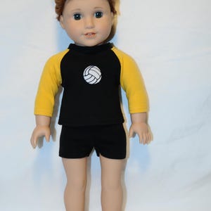 Puede incluir: Una mu&ntilde;eca con cabello rojizo recogido en un mo&ntilde;o, que viste una camiseta negra con mangas amarillas de tres cuartos y un gr&aacute;fico de voleibol blanco en el pecho, junto con pantalones cortos negros. La mu&ntilde;eca tiene piel clara y ojos oscuros.