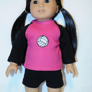 Puede incluir: Una mu&ntilde;eca con cabello largo y negro peinado en dos coletas, que viste una camiseta rosa de manga larga con mangas negras y un gr&aacute;fico de voleibol blanco en el pecho, junto con pantalones cortos negros. La mu&ntilde;eca tiene piel clara y ojos oscuros.