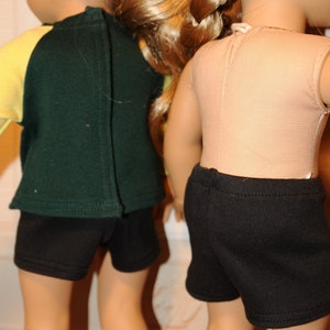 Puede incluir: Dos mu&ntilde;ecas vistas desde atr&aacute;s. La mu&ntilde;eca de la izquierda lleva una camiseta de manga larga verde oscuro y amarilla con pantalones cortos negros. La de la derecha lleva un top beige sin mangas y pantalones cortos negros. Ambas tienen pelo rubio.