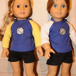 Puede incluir: Dos mu&ntilde;ecas de piel clara con ropa deportiva. La mu&ntilde;eca de la izquierda tiene el pelo largo y rubio y lleva una camiseta azul con mangas amarillas y pantalones cortos negros. La mu&ntilde;eca de la derecha tiene el pelo casta&ntilde;o y lleva una camiseta azul con mangas blancas y pantalones cortos negros. Ambas camisetas tienen un gr&aacute;fico de voleibol blanco en el pecho.