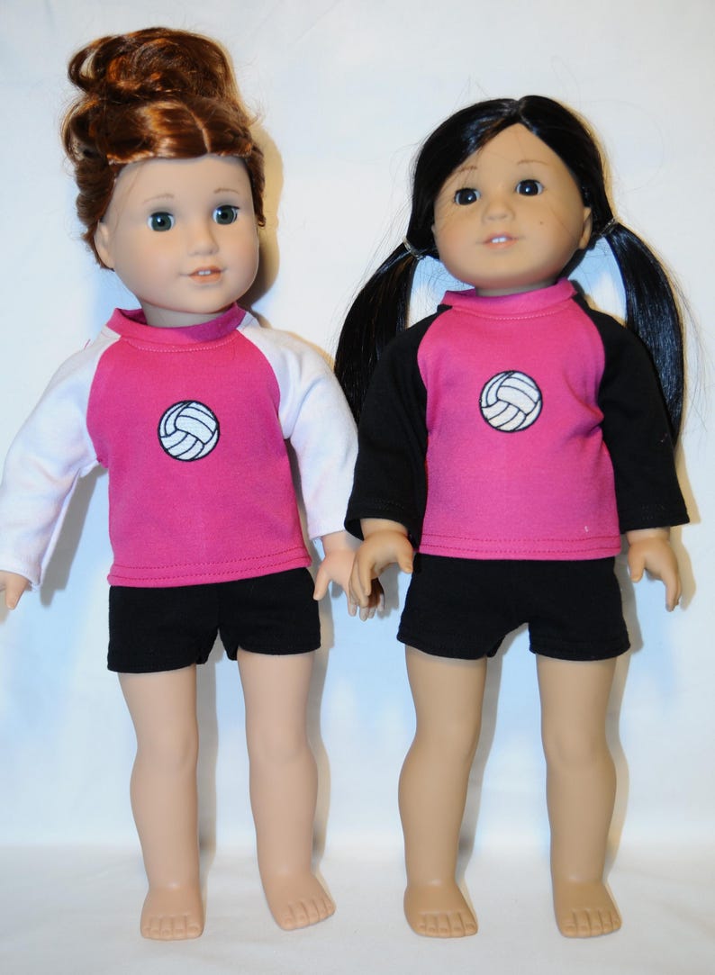 Puede incluir: Dos mu&ntilde;ecas de pie una al lado de la otra. La mu&ntilde;eca de la izquierda tiene el pelo casta&ntilde;o rojizo en un mo&ntilde;o y viste una camiseta rosa con mangas blancas y pantalones cortos negros. La mu&ntilde;eca de la derecha tiene el pelo negro en coletas y viste una camiseta rosa con mangas negras y pantalones cortos negros. Ambas camisetas tienen un peque&ntilde;o gr&aacute;fico de voleibol blanco en el pecho.