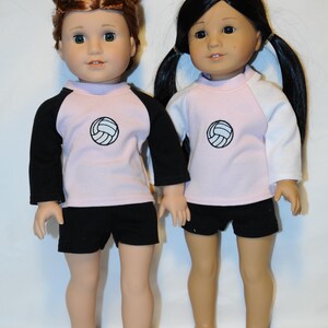 Puede incluir: Dos mu&ntilde;ecas de pie una al lado de la otra, ambas con camisetas de color rosa claro con un gr&aacute;fico de voleibol negro en el pecho. La mu&ntilde;eca de la izquierda tiene el pelo casta&ntilde;o rojizo y mangas negras, mientras que la de la derecha tiene el pelo negro y mangas blancas. Ambas mu&ntilde;ecas llevan pantalones cortos negros.