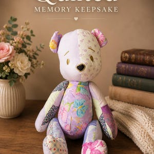 May include: A stuffed bear made of various quilted fabric patches in shades of purple, pink, and white with butterfly and floral patterns. The bear has a black heart-shaped nose and embroidered eyes. Text above reads Quilted MEMORY KEEPSAKE.