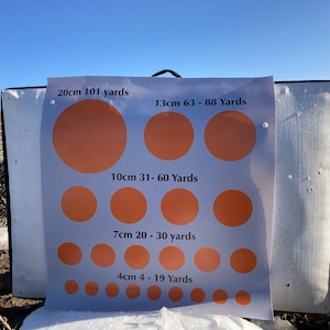 May include: A white target with orange circles of varying sizes. The target is labeled with the size of each circle in centimeters and the corresponding yardage. The text reads: 20cm 101 yards, 13cm 63-88 Yards, 10cm 31-60 Yards, 7cm 20-30 yards, 4cm 4-19 Yards.