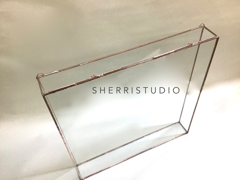 May include: A clear glass box with a copper frame. The box has a shelf inside and is designed to hang on a wall. The text "SHERRISTUDIO" is visible on the front of the box.