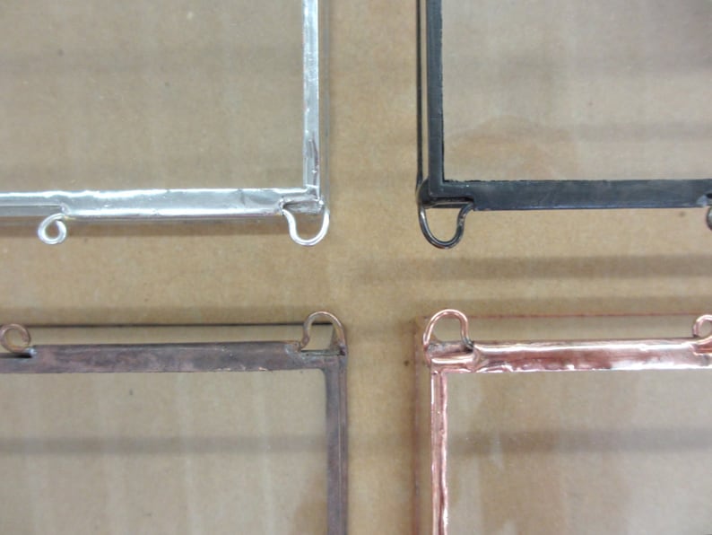 May include: Four square picture frames with glass panes and metal frames. The frames are silver, black, copper, and brown. Each frame has two hanging loops.
