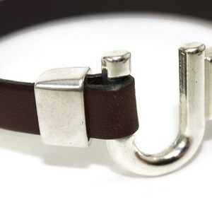May include: A brown leather bracelet with a silver clasp. The clasp is shaped like a U and has a small silver piece on the top.
