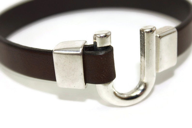May include: A brown leather bracelet with a silver clasp. The clasp is shaped like a U and has a small silver piece on the top.