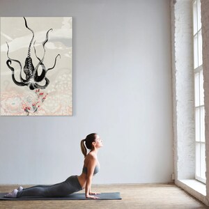 K&ouml;nnte beinhalten: Eine Frau in einem grauen Yoga-Outfit macht eine Kobra-Pose auf einer grauen Yogamatte vor einer wei&szlig;en Wand mit einem schwarz-wei&szlig;en Kraken-Druck, der daran h&auml;ngt. Der Raum hat ein gro&szlig;es Fenster mit wei&szlig;en Ziegeln drumherum.