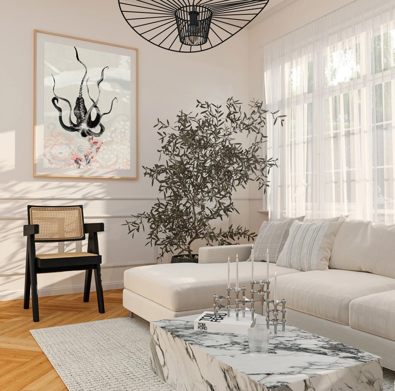 K&ouml;nnte beinhalten: Ein wei&szlig;es Sofa mit einem schwarz-wei&szlig; gemusterten Kissen und einem schwarz-wei&szlig;en Buch mit dem Titel "TOM FORD" auf einem wei&szlig;en Marmor-Couchtisch. Auf dem Tisch steht ein schwarzer Metall-Kandelaber mit sechs Kerzen. Im Vordergrund steht ein schwarzer Stuhl mit Rohrgeflecht. Ein schwarz-wei&szlig; gerahmtes Bild mit einer Darstellung eines Kraken h&auml;ngt an der Wand.