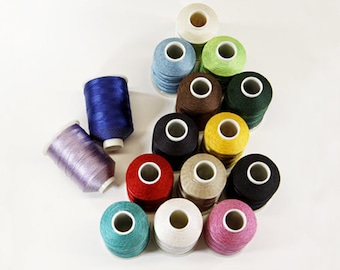 May include: Assortment of 14 spools of thread in various colors, including blue, green, brown, yellow, red, black, white, and purple. The spools are arranged in a circle on a white surface. The text "PACIFIC TRIMMING" is visible in the top right corner of the image.