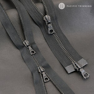 May include: Two black zipper tapes with metal teeth and sliders. The zippers are laid out on a dark gray surface.