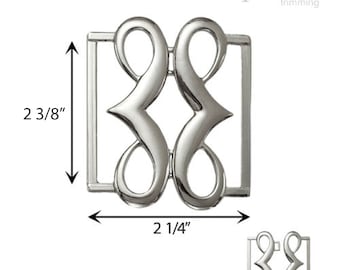 Puede incluir: Hebilla de metal plateado con un diseño decorativo. La hebilla mide 6 cm de alto y 5,7 cm de ancho.