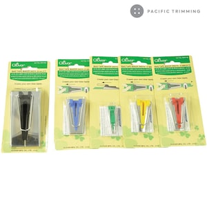 May include: Five Clover Bias Tape Makers in different colors, each with a clear plastic package. The packages have instructions for creating bias tape in English, Spanish, German, and French. The packages are on a white background.