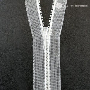May include: A close-up of a white zipper with a silver slider. The zipper is on a black background.