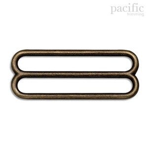 May include: Antique gold metal slider buckle with two loops. This buckle is used for adjusting the length of straps or belts.