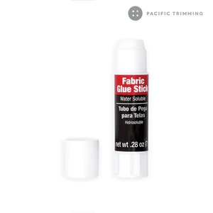 Puede incluir: Un tubo de pegamento para tela de pl&aacute;stico blanco con una etiqueta negra que dice "Fabric Glue Stick" y "Water Soluble". La etiqueta tambi&eacute;n dice "Tubo de Pega para Telas" y "Hidrosoluble". El tubo tiene una tapa blanca y el peso neto es de 28 oz (7 g).