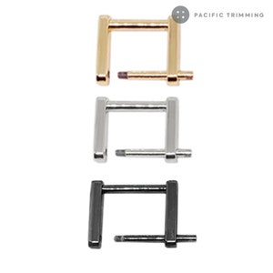 Könnte beinhalten: Drei quadratische Metallschnallen mit einem Stift. Die Schnallen sind golden, silber und schwarz.