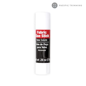 Puede incluir: Tubo blanco de pegamento para tela con texto rojo y negro que dice "Fabric Glue Stick", "Water Soluble", "Tubo de Pega para Telas" e "Hidrosoluble". El tubo est&aacute; etiquetado con "Net wt. 28 oz (7.9".
