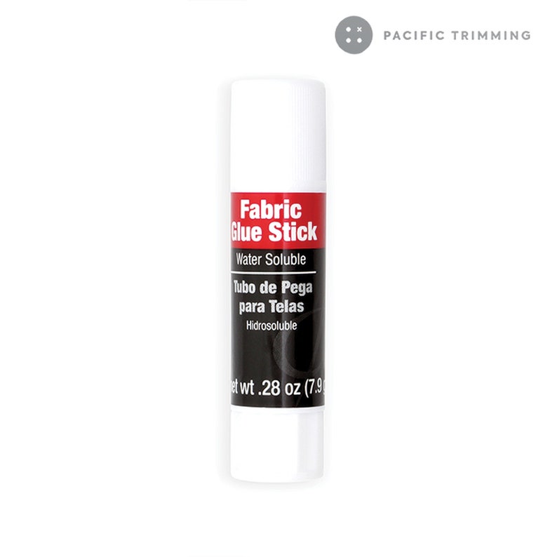 Puede incluir: Tubo blanco de pegamento para tela con texto rojo y negro que dice "Fabric Glue Stick", "Water Soluble", "Tubo de Pega para Telas" e "Hidrosoluble". El tubo est&aacute; etiquetado con "Net wt. 28 oz (7.9".