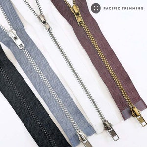 以下が含まれることがあります： 金属製の歯とスライダーが付いた、異なる4種類のジッパーテープ。テープは黒、グレー、白、茶色。スライダーは金と銀。画像の右上に「PACIFIC TRIMMING」の文字が見える。